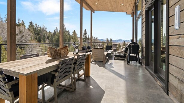 A wooden deck with a dining table and chairs, a grill, and a view of the surrounding forest. - Mountain Modern Retreat w/Hot Tub (Victor)