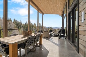 Eine Holzterrasse mit Esstisch und Stühlen, einem Grill und Blick auf den umliegenden Wald.