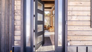 A wooden exterior with a black-framed door leading to an interior with a dining area and a view of trees. - Mountain Modern Retreat w/Hot Tub (Victor)