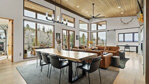 A spacious living area with a wooden ceiling, large windows, and a dining table. - Mountain Modern Retreat w/Hot Tub (Victor)