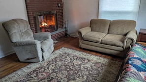 Una sala de estar con chimenea de ladrillo, dos sillones, un sofá y una alfombra estampada.
