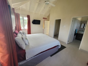 A bedroom with a large bed, a TV mounted on the wall, and a ceiling fan.