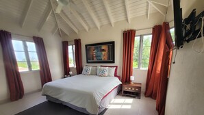 Une chambre à coucher avec un grand lit, une table de chevet, un téléviseur fixé au mur et une fenêtre avec des rideaux.