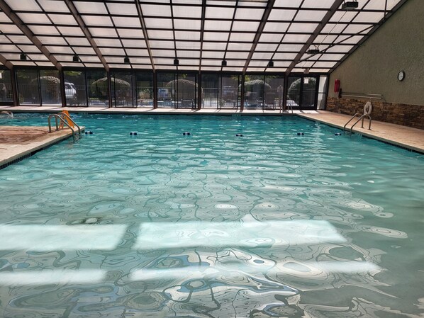 Ein Hallenbad mit klarem Wasser, gefliestem Boden und einer Dachkonstruktion.