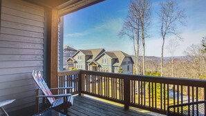 A wooden deck with a glass table and two chairs, overlooking a row of houses and a mountain view. - Townhome Echota Available10/21 Sleeps 8 HotTub/Pool SEE SPECIALS in Description  (Banner Elk)