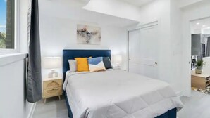 A modern bedroom with a large bed, a nightstand, a bedside table, and a ceiling light. - Luxury New Condo By Niagara Falls (Niagara Falls)