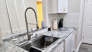 A kitchen with a granite countertop, stainless steel sink, and white cabinets.