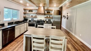 A kitchen with wooden cabinets, a stainless steel refrigerator, and a dining table with chairs. - Mountainside Luxury Cottage 2—LOCATION! LOCATION! (Mena)