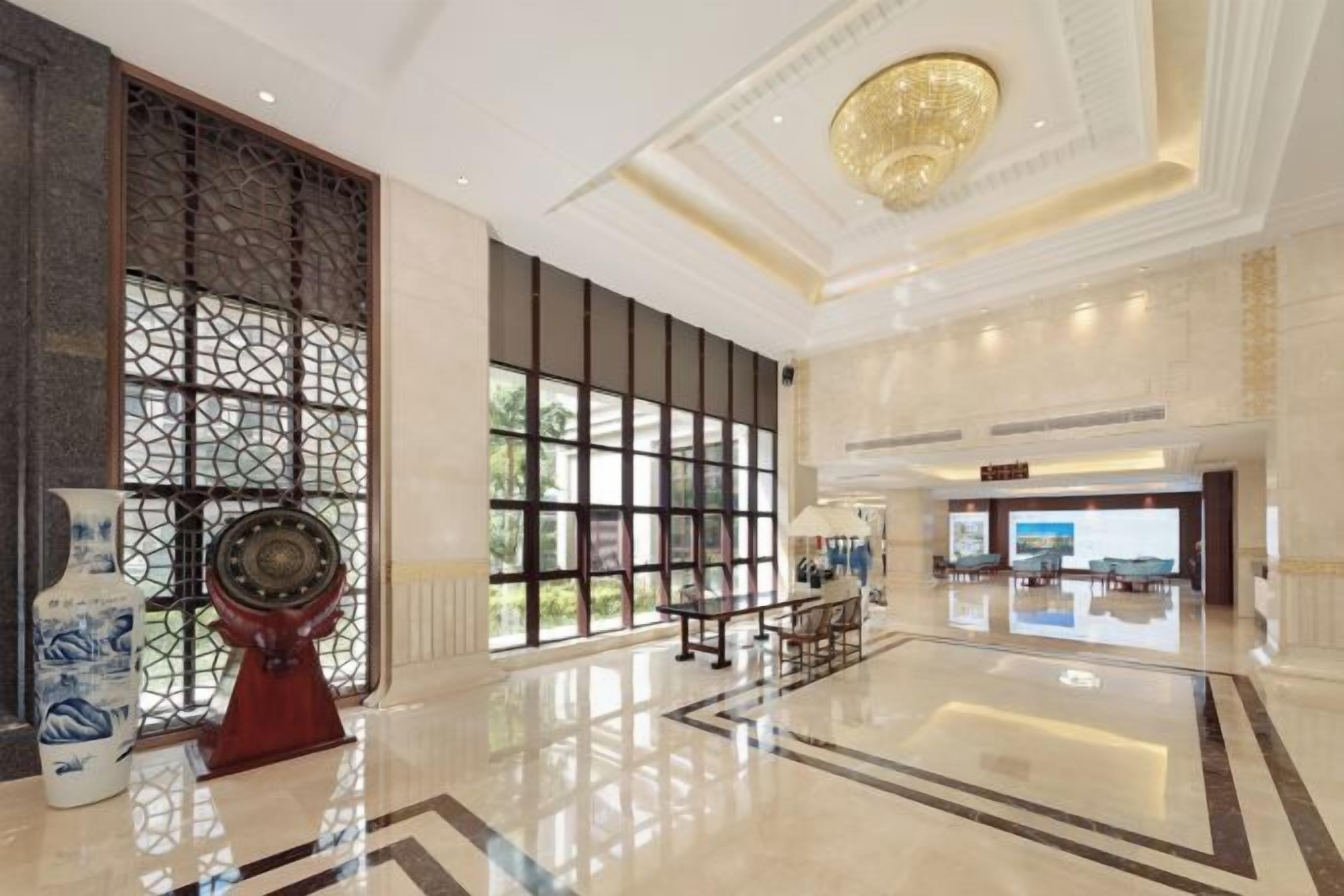 A spacious lobby with a large chandelier, a reception desk, and a view of the outdoors through large windows.