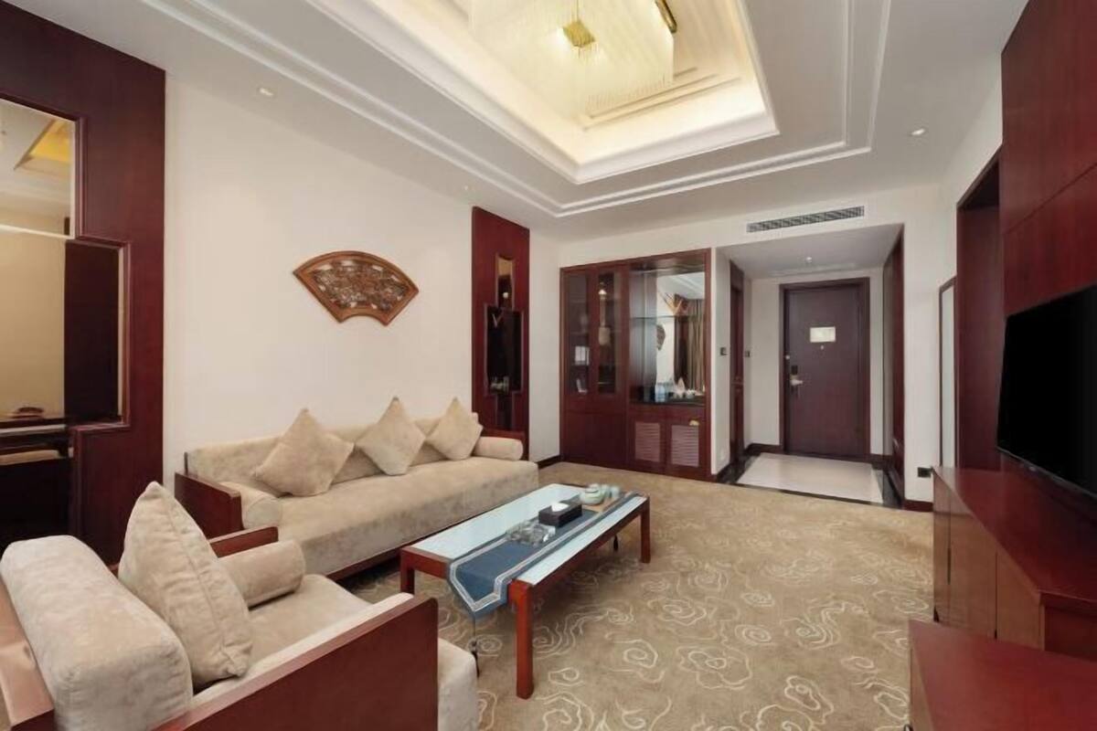 A living room with a sofa, coffee table, and a television. There is a door leading to another room and a ceiling light fixture.