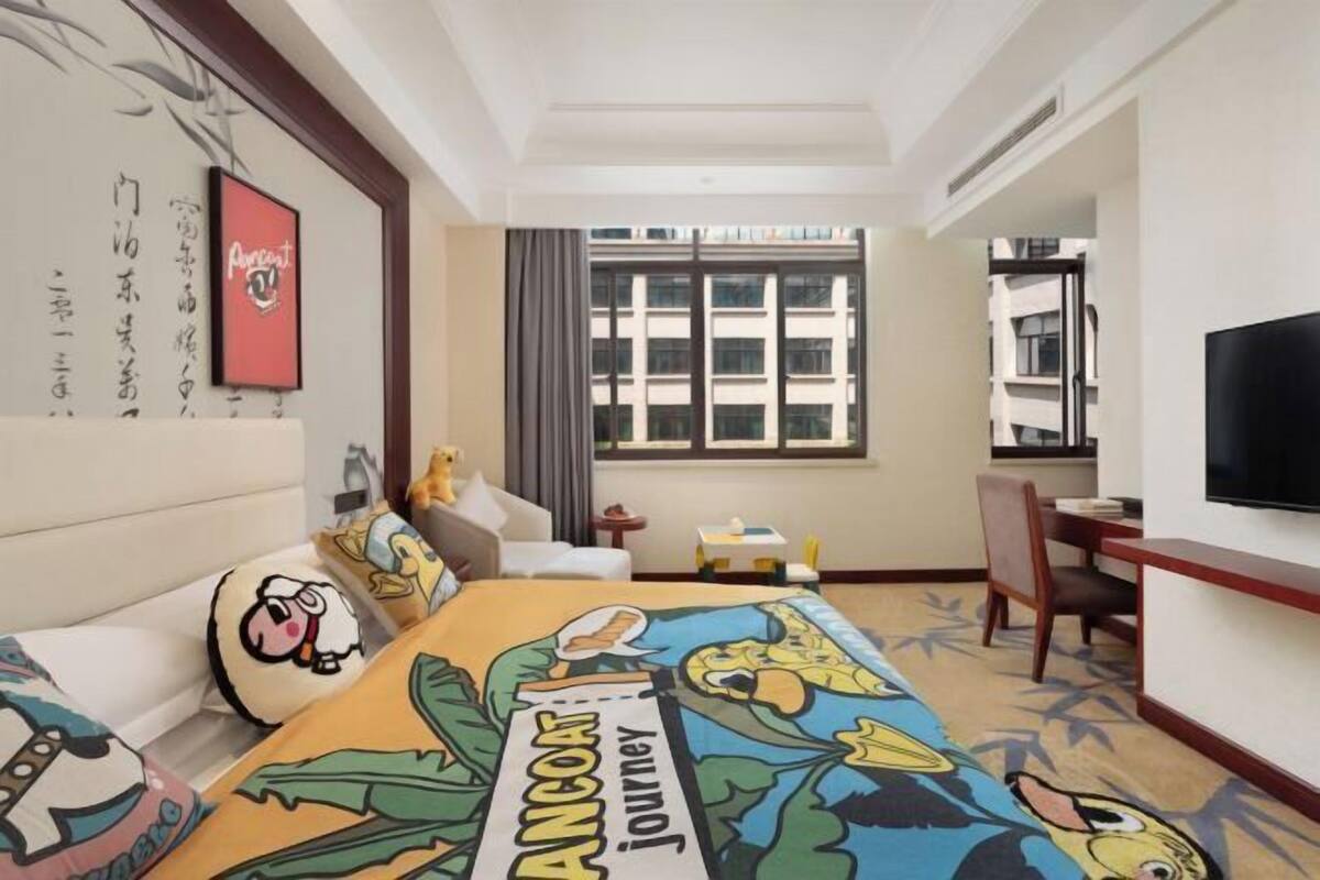 A hotel room with a bed, a desk, a chair, a TV, and a window with a view of buildings.