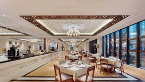 Un vaste espace de restauration dans l’hôtel, avec de nombreuses tables et chaises, un long comptoir où est présenté un buffet, et de grandes fenêtres offrant une vue panoramique.