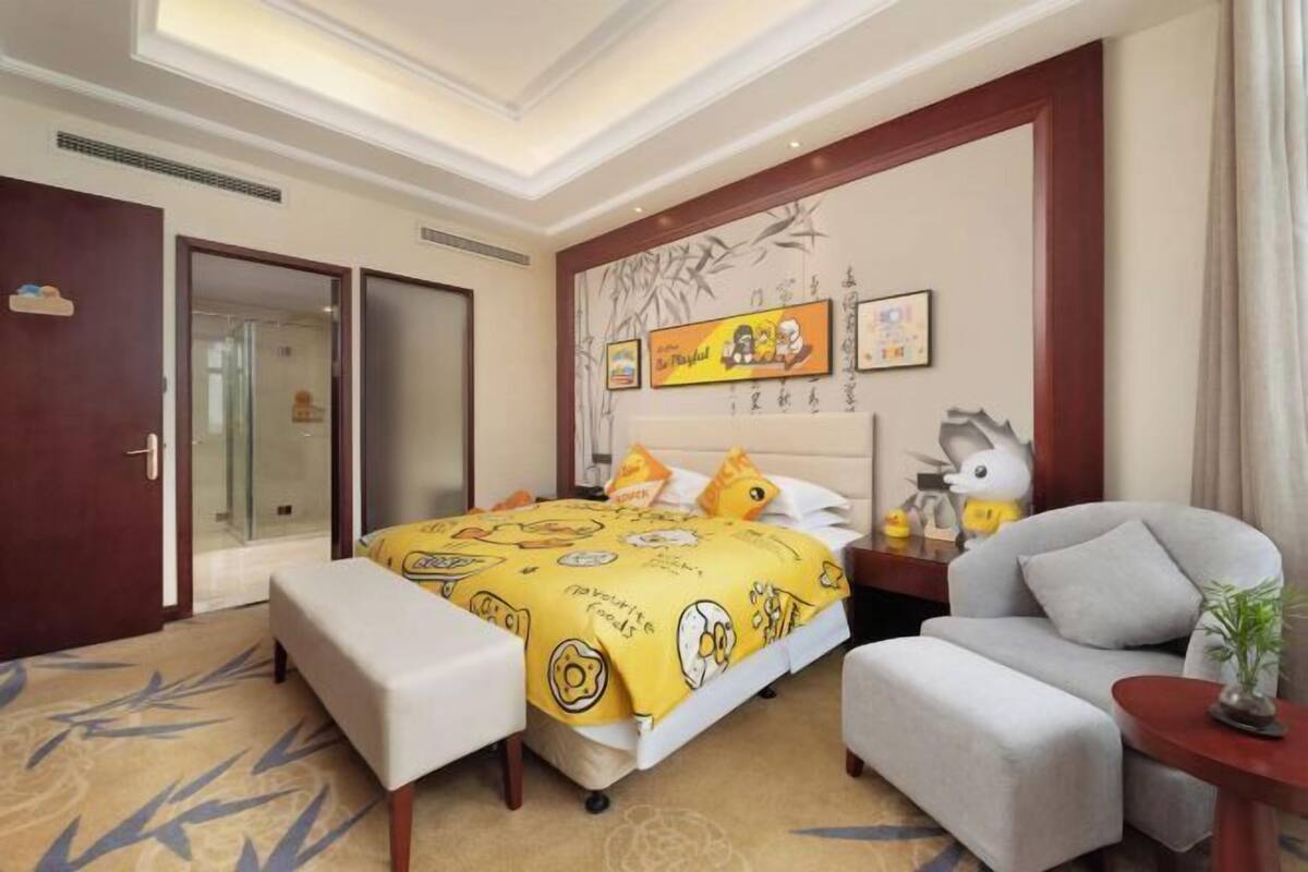 A hotel room with a bed, a sofa, a bench, a bedside table, a wall with artwork, and a door.