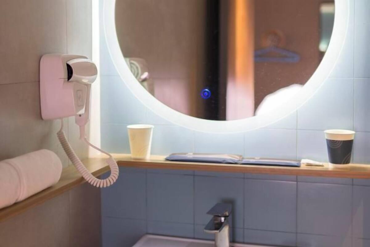 A bathroom with a round mirror, a hairdryer, a towel, and two cups on the counter.