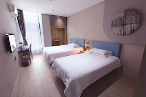 Habitación de hotel con dos camas, un escritorio con silla, televisor y un ventanal con cortinas.