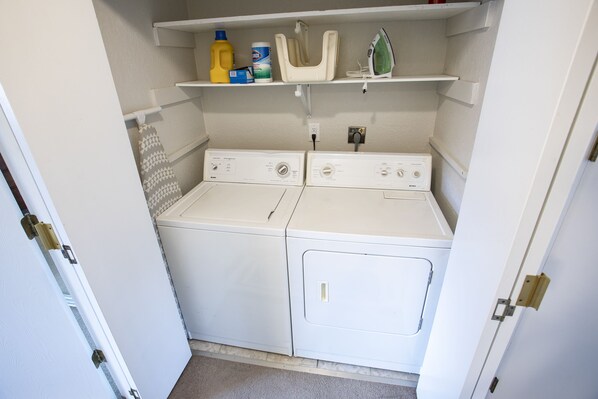 A compact laundry room with two white washing machines and a shelf above containing cleaning supplies. - NEW LISTING! Adventure and Unwind:View of Mountains, Near AirP, Lake w 2 Kayaks (Anchorage)