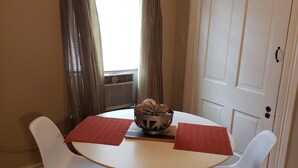 Un comedor con una mesa redonda, dos sillas blancas, un mantel individual rojo y un cuenco decorativo.