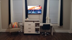 Una habitación con escritorio, silla, televisión y sofá.