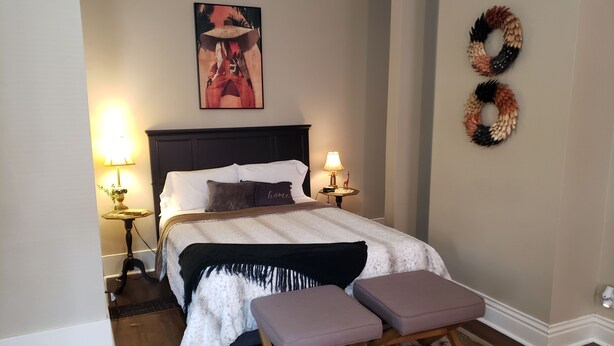 Un dormitorio con una cama, dos mesitas de noche con lámparas, una obra de arte en la pared y un adorno decorativo.
