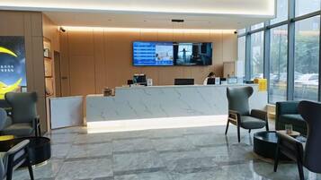A hotel reception area with a reception desk, seating, a large window, and a television screen.
