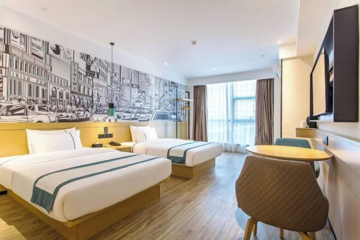 Una habitación de hotel con dos camas, una mesa redonda, una silla y un mural grande en la pared.
