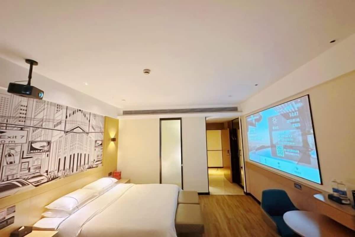 Habitación de hotel con cama, escritorio, pantalla de proyector y un mural de paisaje urbano en la pared.
