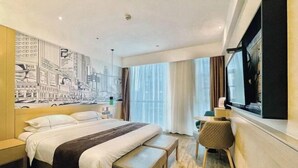 Habitación de hotel con una cama grande, un escritorio, una silla, un televisor y un mural con vista a la ciudad.