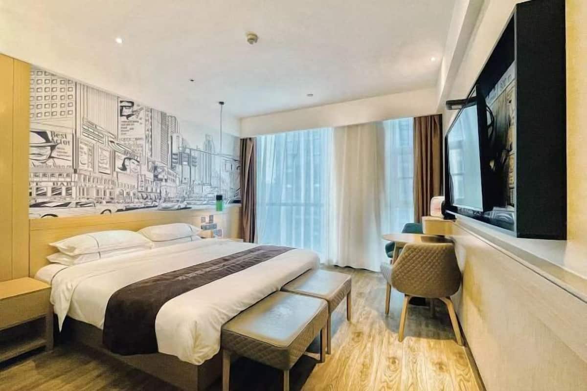 Habitación de hotel con una cama grande, un escritorio, una silla, un televisor y un mural con vista a la ciudad.