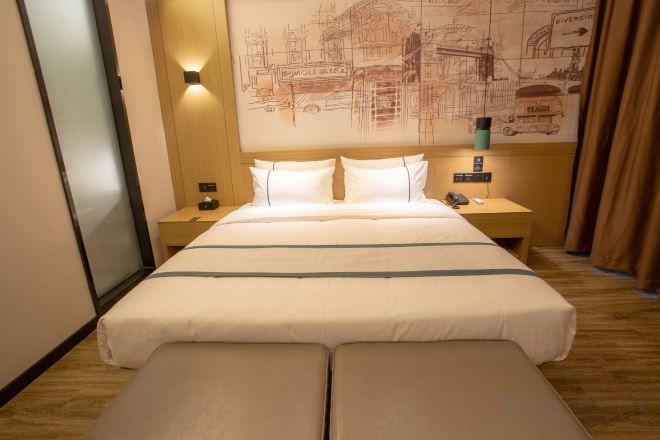 Una habitación de hotel con una cama grande, mesitas de noche, una lámpara de pared y un ventanal con cortinas.