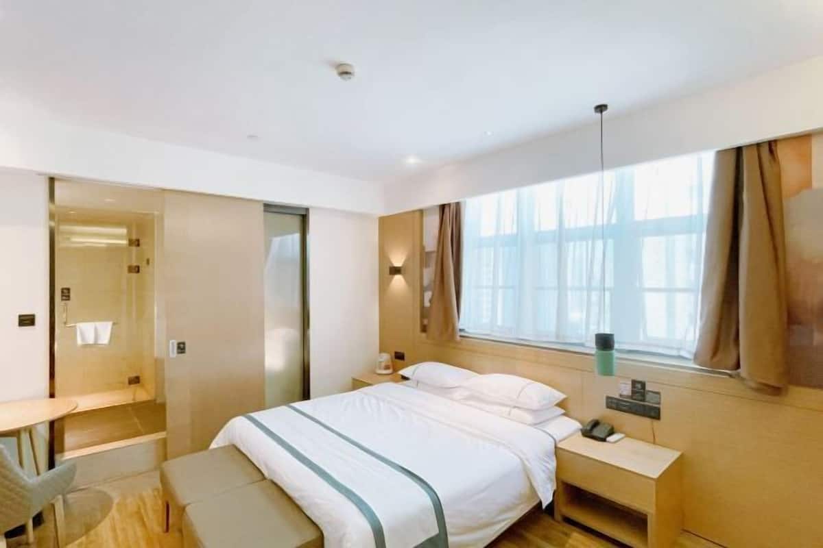Una habitación de hotel moderna con cama, mesita de noche, lámpara y vistas al exterior a través de una ventana.