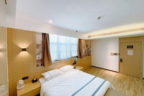 A hotel room with a bed, bedside table, nightstand, window with curtains, and a door.