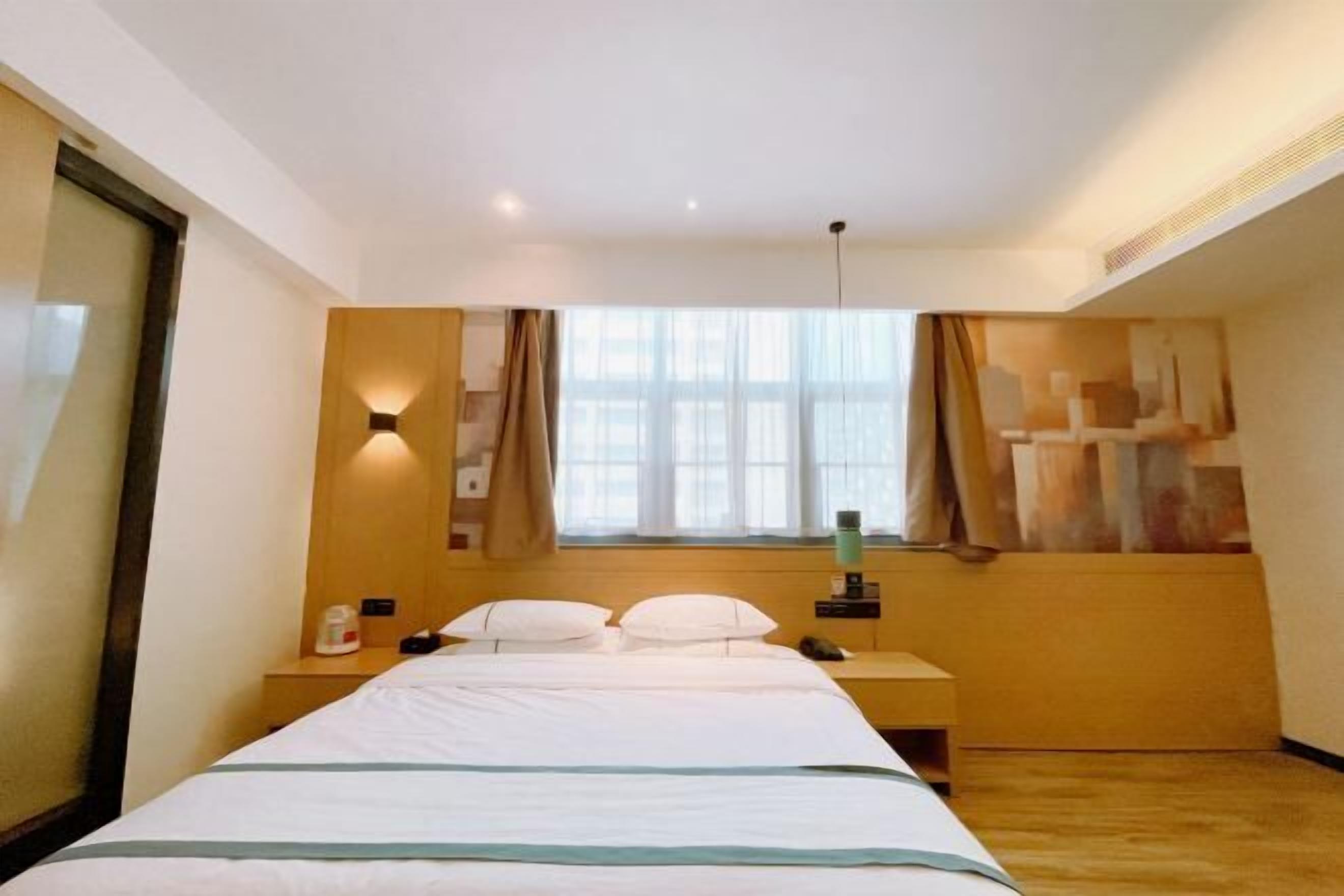 Una habitación de hotel con cama, mesita de noche, lámpara y ventana con cortinas.