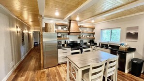 A modern kitchen with wooden beams, a stainless steel refrigerator, wooden cabinets, and a dining area with a table and chairs. - Mountainside Luxury Unit 3—LOCATION! LOCATION! (Mena)