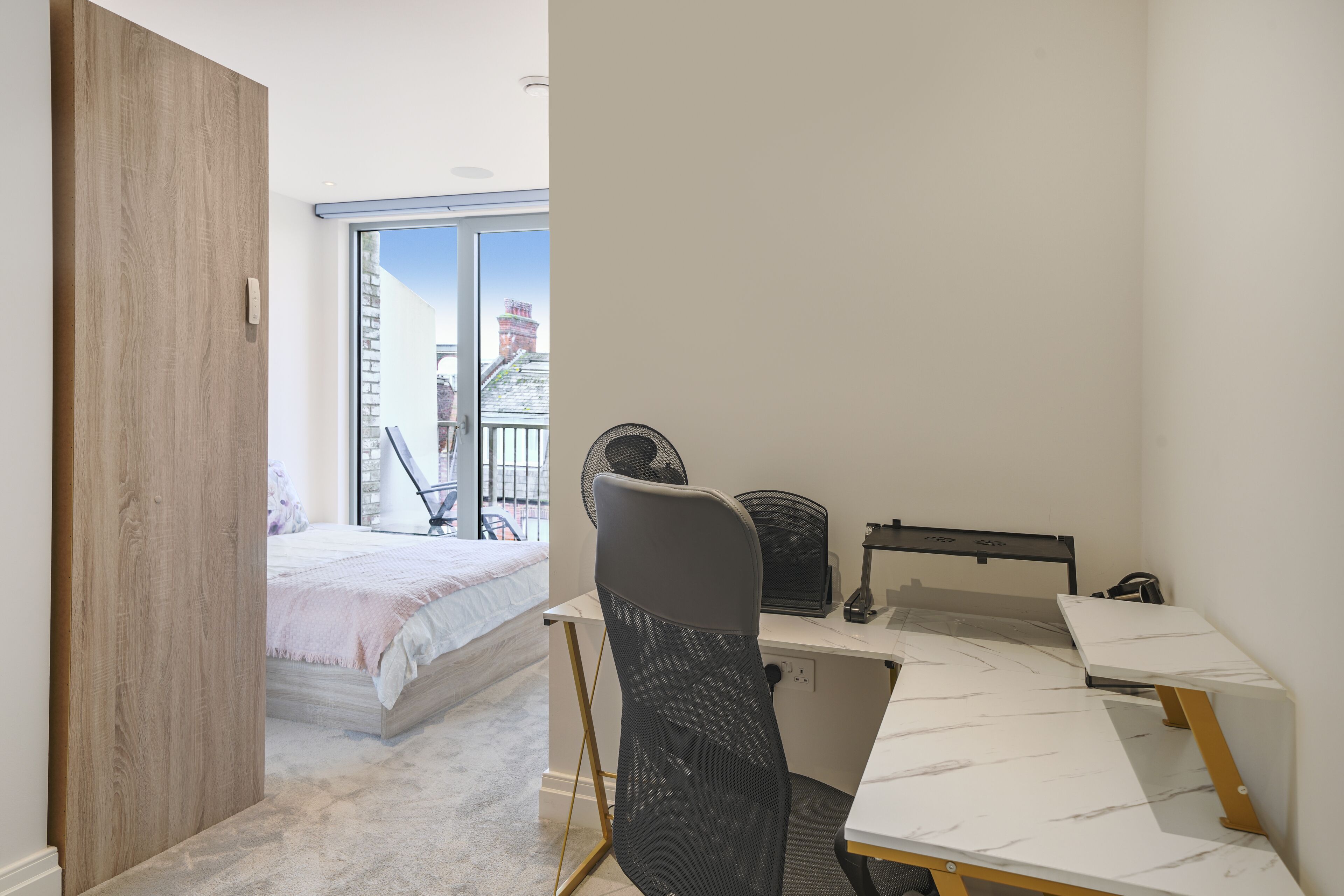 Un dormitorio con cama, un escritorio con silla y una ventana con vista a edificios.