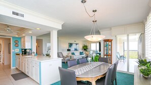 Uma cozinha espaçosa com ilha central, área de jantar com mesa grande e cadeiras, e sala de estar com sofá e mesa de centro.