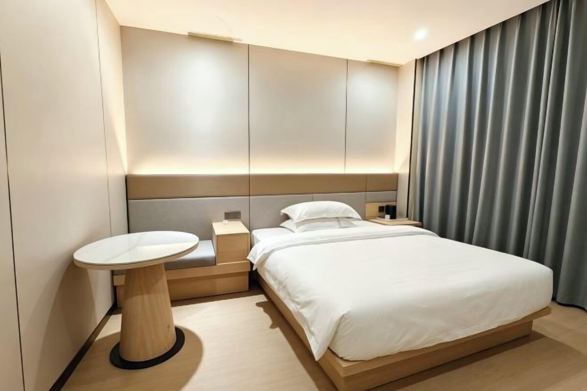 A modern hotel room with a large bed, bedside table, and a small round table.