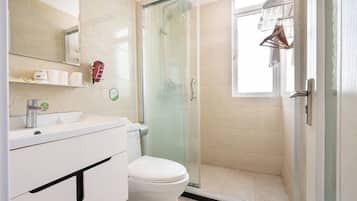 Een moderne badkamer met een douche in een glazen cabine, een toilet en een wastafel met spiegel erboven.
