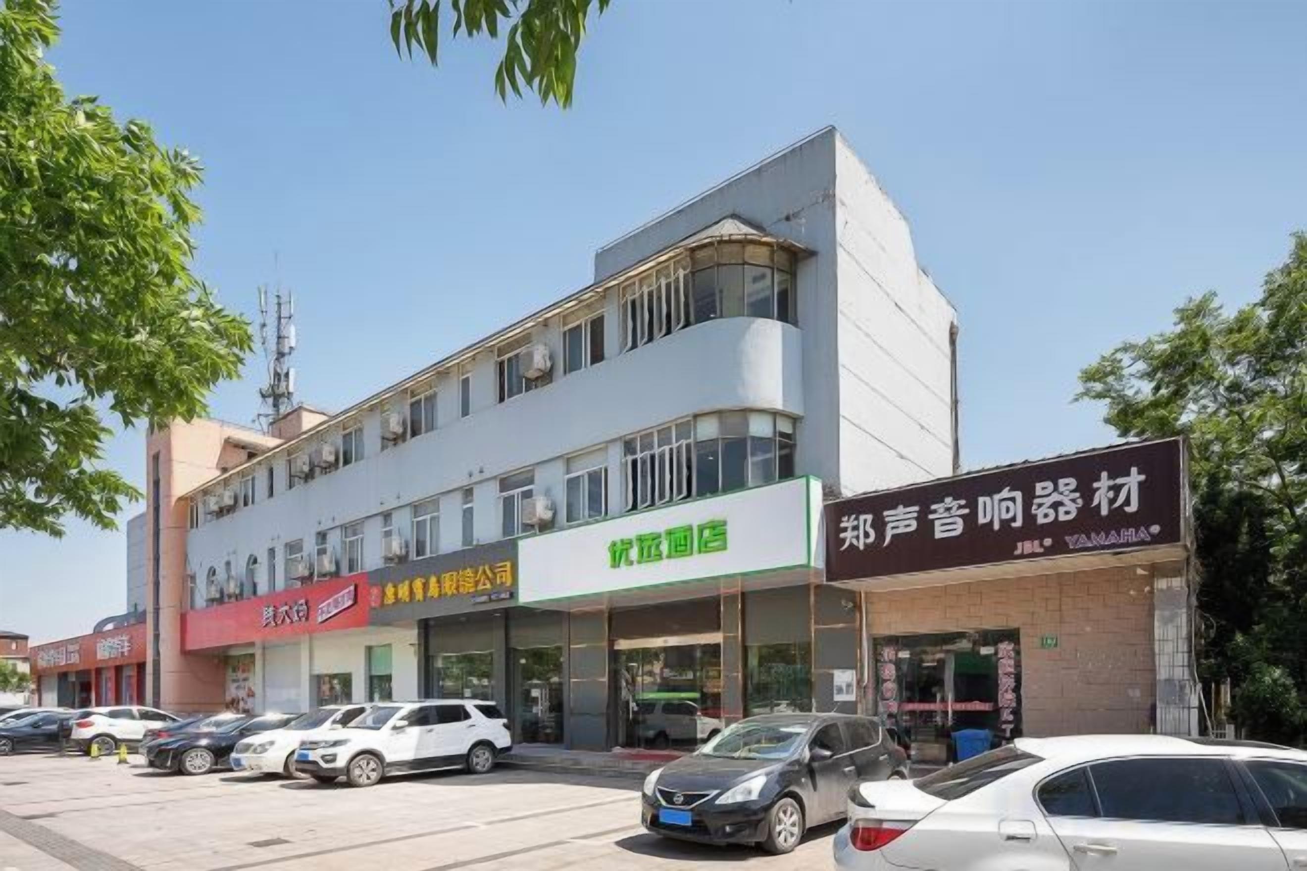A multi-story building with commercial signage, a parking lot, and several parked cars.