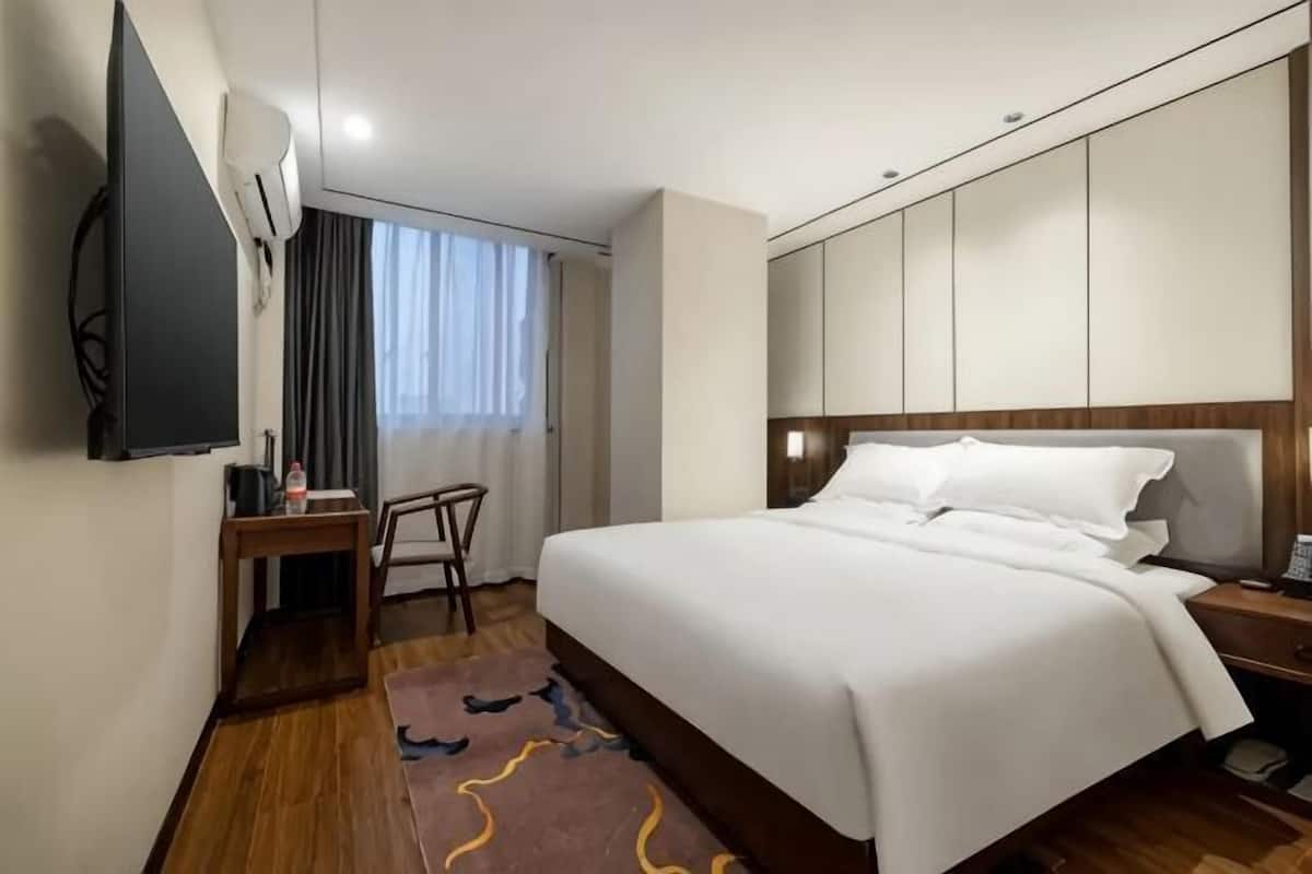 A hotel room with a bed, a desk, a chair, a TV, and a window with curtains.