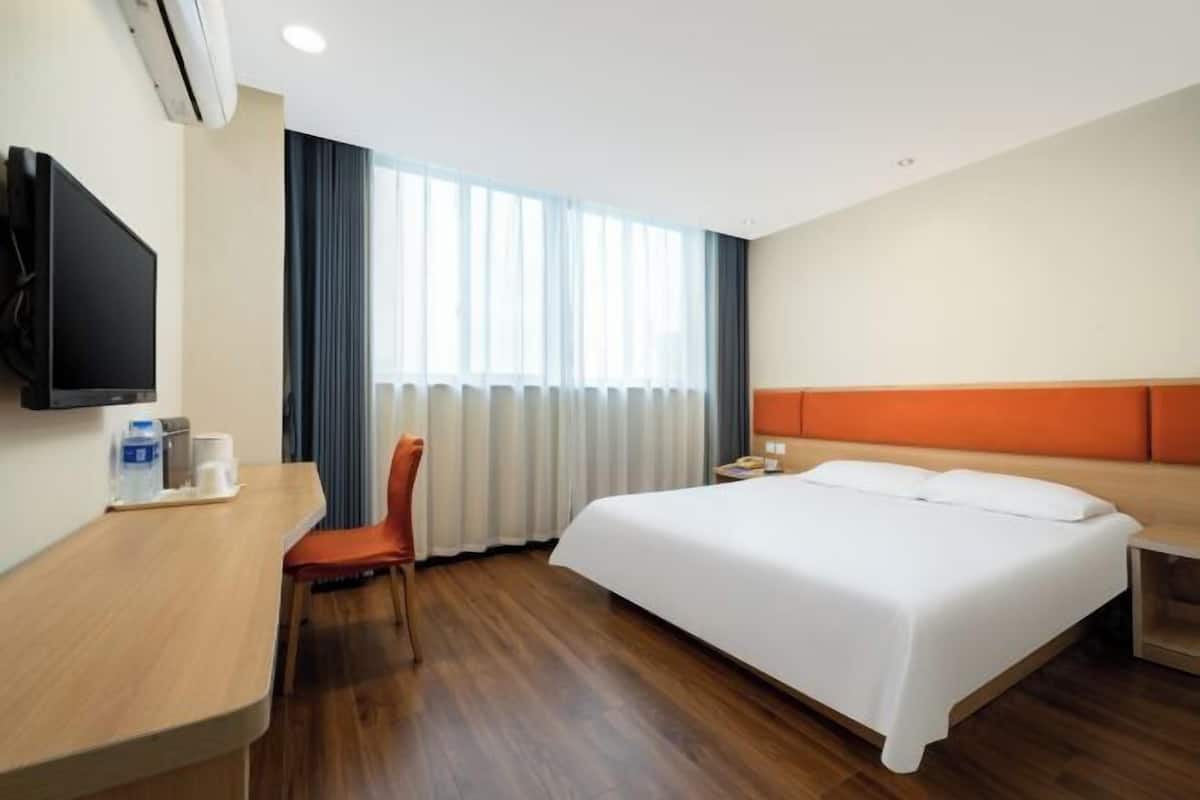 A hotel room with a bed, a desk, a chair, a TV, and a window with curtains.