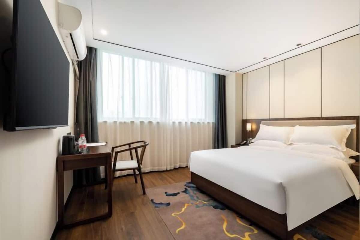 A hotel room with a bed, a desk, a chair, a TV, and a window with curtains.