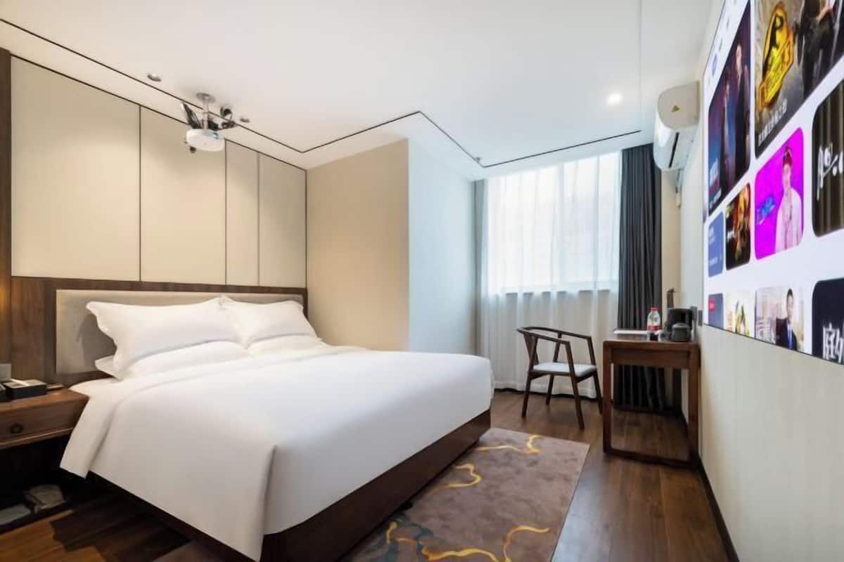 A modern hotel room with a large bed, a desk, and a wall with photos.