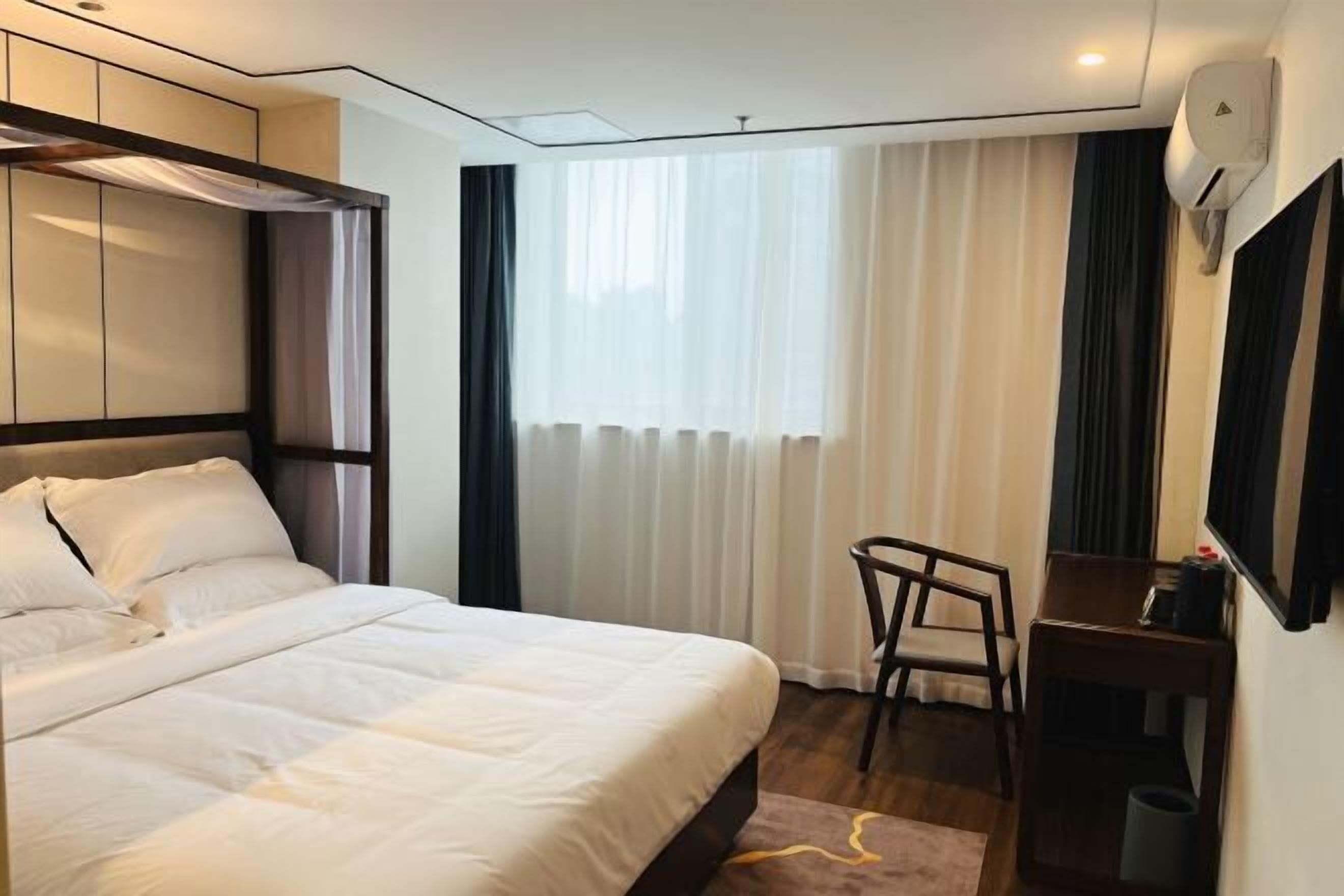 A hotel room with a bed, a desk, a chair, a TV, and a window with curtains.