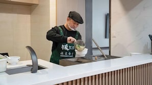 A person in a green apron preparing food at a counter with a sink and a bowl. - YFT Hotel (Haichang South Road Yintaicheng Branch) (Haining)