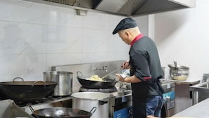 A chef cooking in a professional kitchen with stainless steel appliances and a tiled backsplash. - YFT Hotel (Haichang South Road Yintaicheng Branch) (Haining)