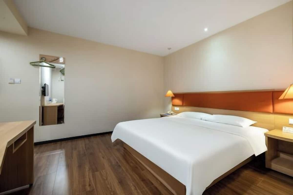 A hotel room with a bed, bedside table, lamp, and a mirror.
