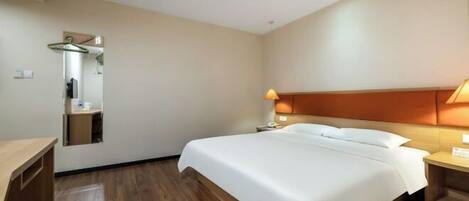 A hotel room with a bed, bedside table, lamp, and a mirror.