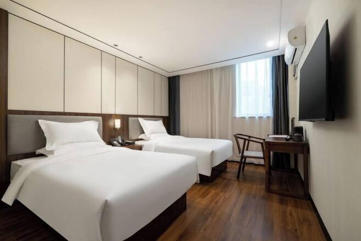 A hotel room with two beds, a desk, a chair, a TV, and a window with curtains.