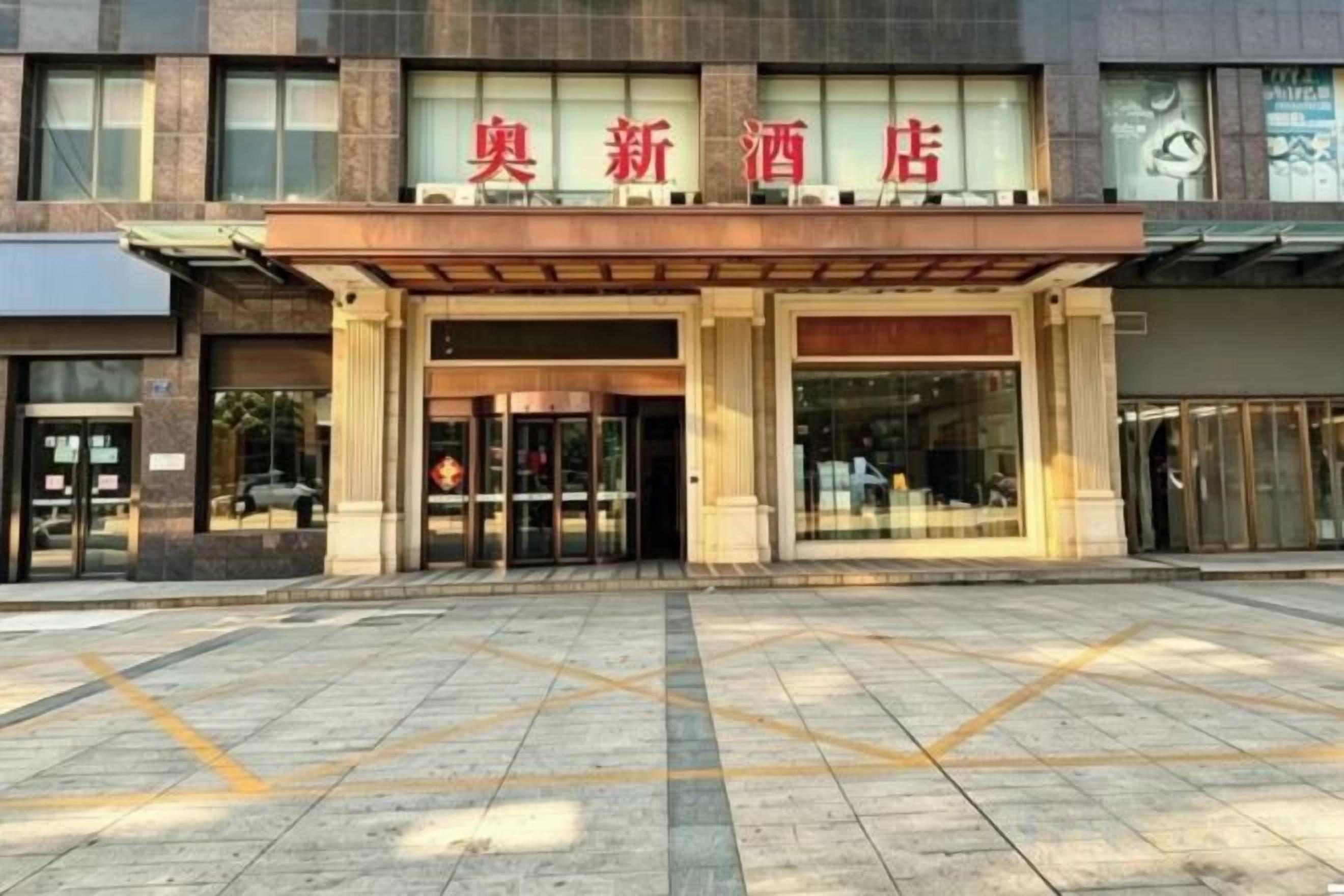 A hotel entrance with a sign above the doors, a tiled pavement, and a clear sky.