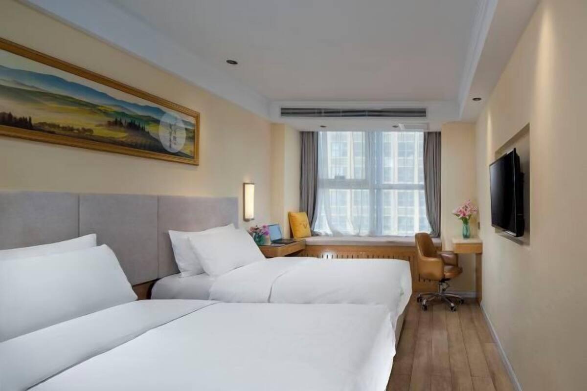 Habitación de hotel con dos camas, un escritorio con silla, televisor y ventana con cortinas.